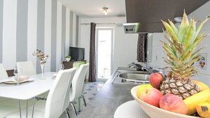 Une cuisine moderne avec un coin repas, comprenant un grand saladier de fruits, un téléviseur et des murs à rayures.