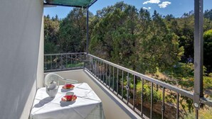 Varanda com mesa posta para dois, com vista para uma área arborizada.