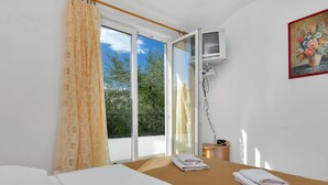 Quarto de hotel com cama, uma mesinha com toalhas, janela com cortinas e um quadro na parede.