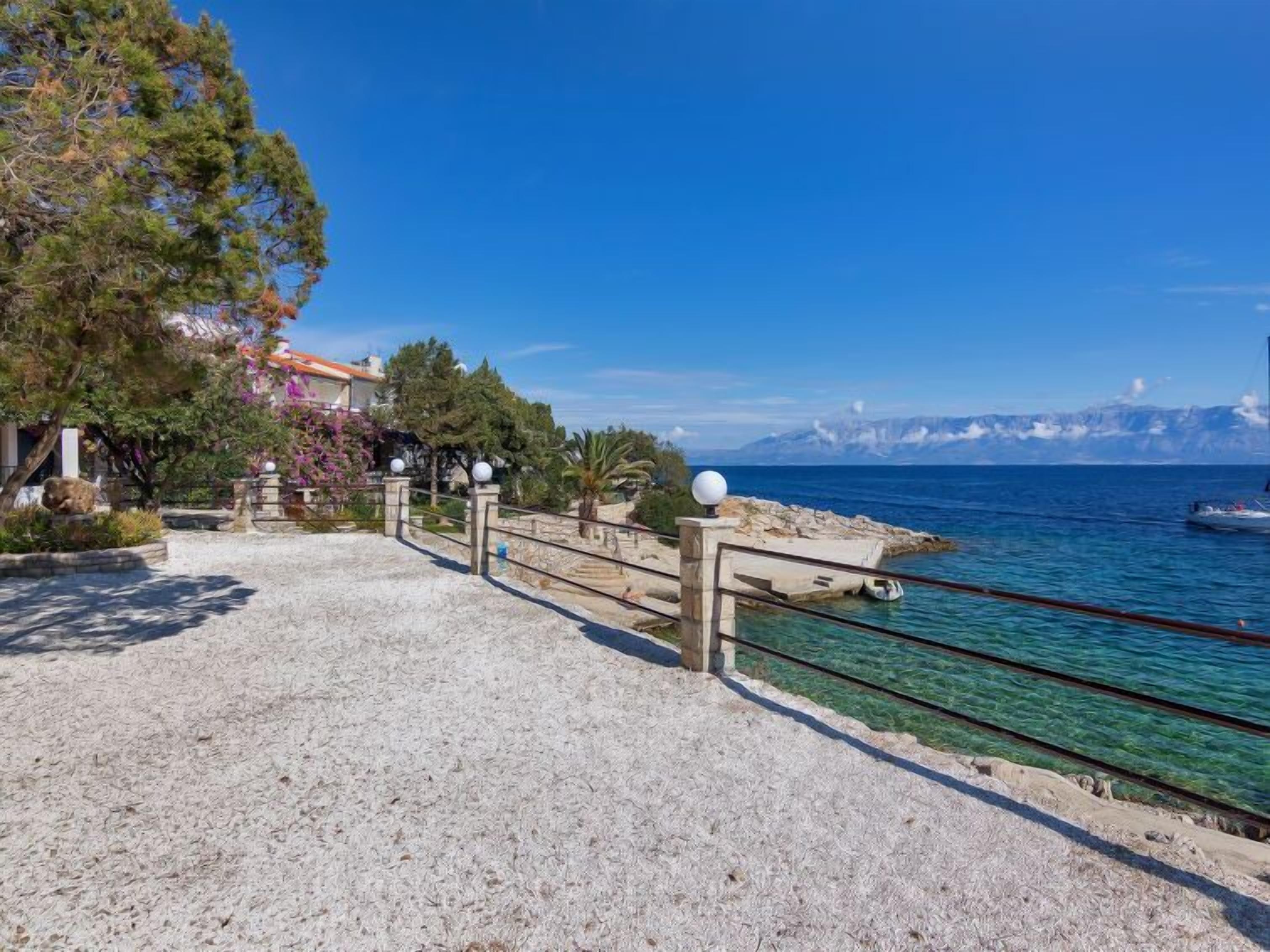 A coastal walkway with clear sea views, a rocky shoreline, and a mountainous backdrop.