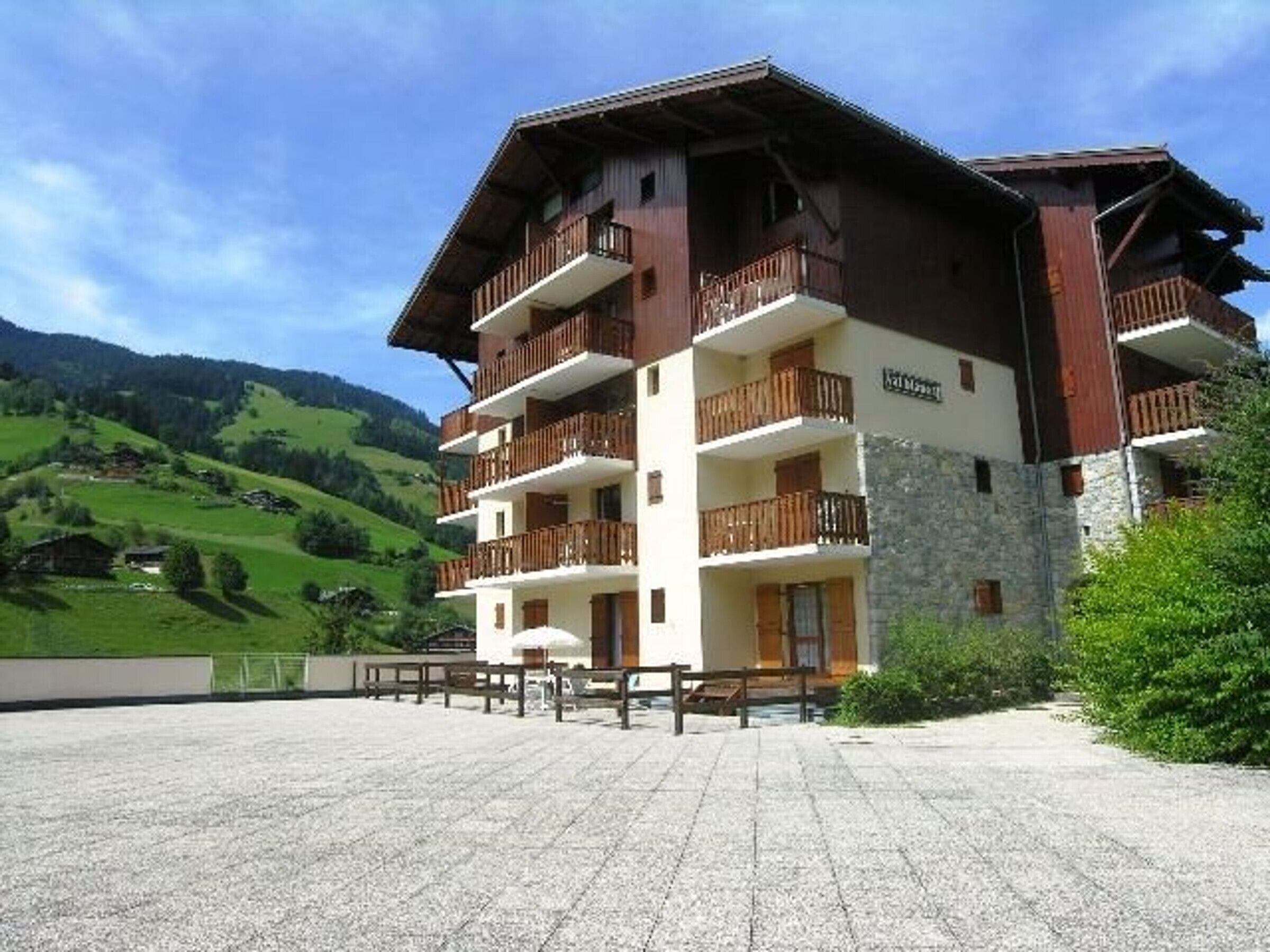 A multi-story building with balconies, set against a mountainous backdrop.