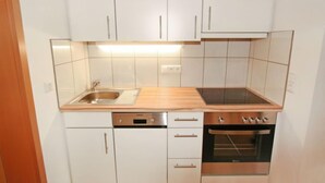 Ett kompakt kök med vita skåp, en diskho i rostfritt stål, en inbyggd ugn och en diskmaskin.