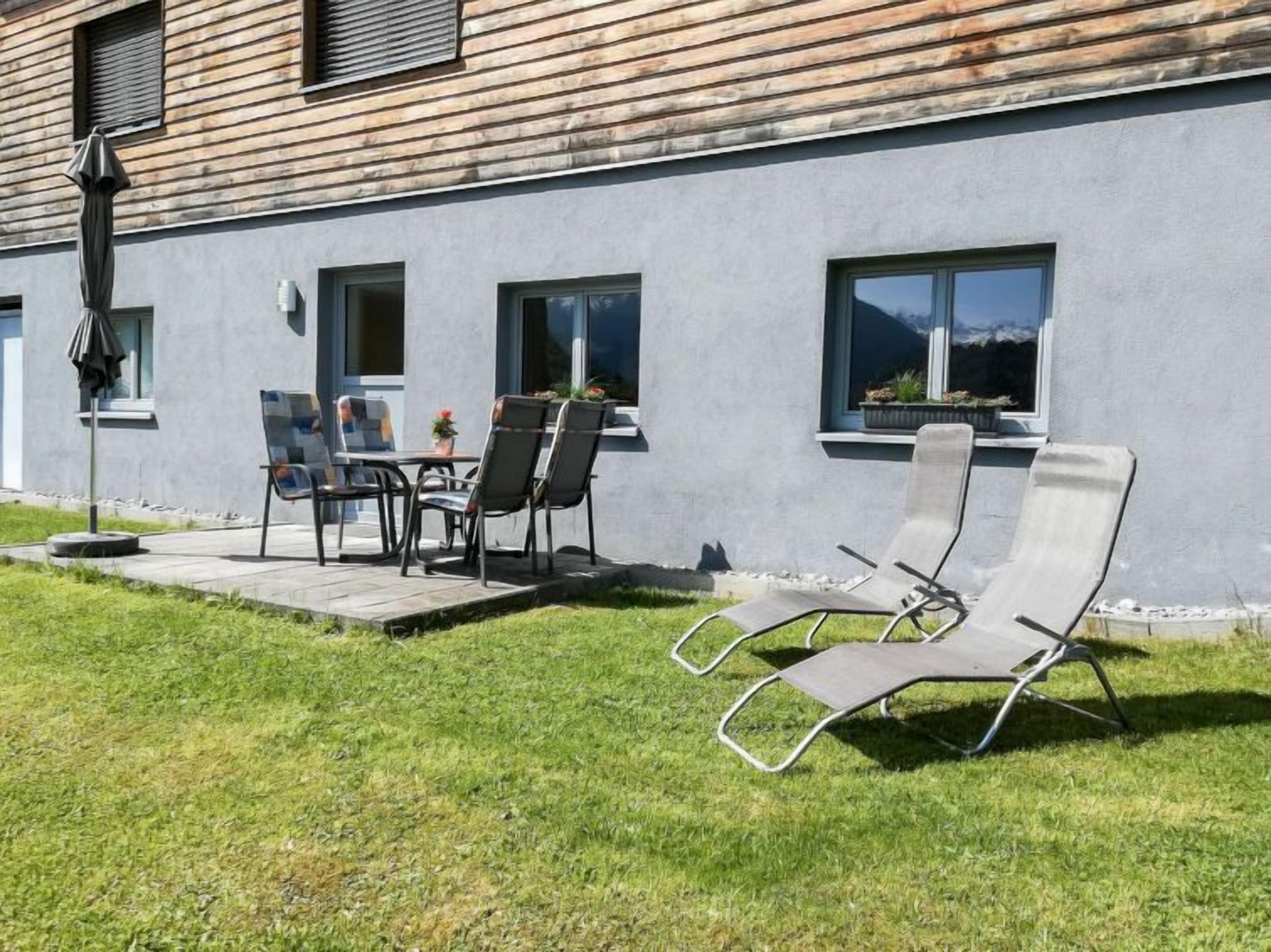 Ein modernes Gebäude mit grauer Fassade, einer Terrasse mit Außenmöbeln und einem Rasen.