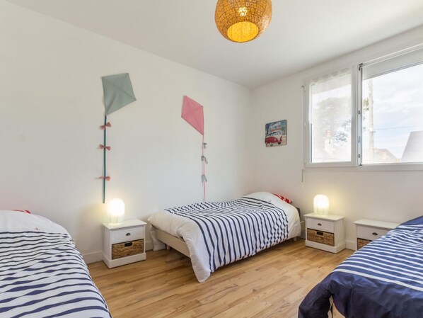 Un dormitorio con dos camas, suelo de madera, mesitas de noche con lámparas y una ventana con vistas.