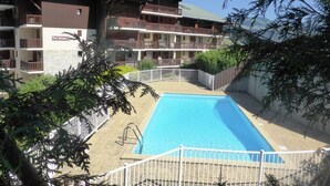 Un hotel con piscina, varios balcones y montañas al fondo.