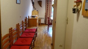 Un pasillo con sillas de madera y una mesa, un reloj en la pared y una puerta que da a otra habitación.