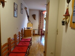 Un corridoio con sedie e tavolo di legno, un orologio appeso al muro e una porta che dà su un'altra stanza.