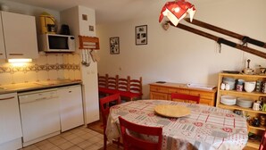 Cuina compacta amb zona de menjador, que compta amb microones, rentaplat i armaris de fusta.