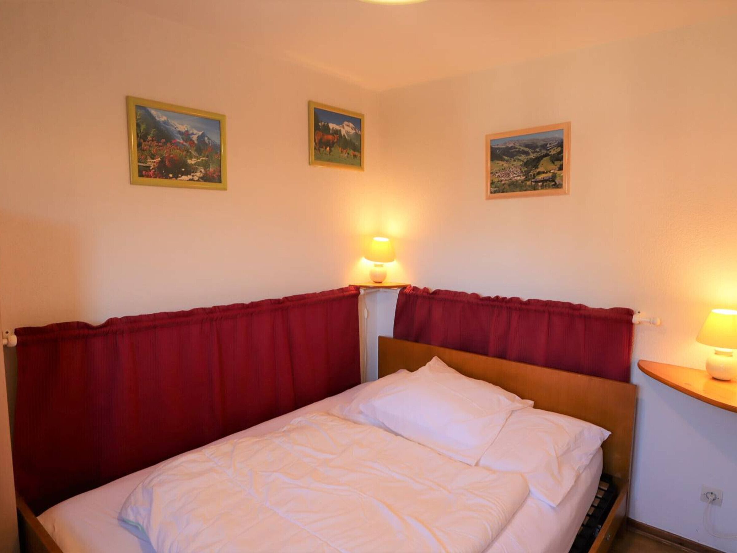 Une chambre d’hôtel avec un lit, des rideaux rouges et trois tableaux encadrés accrochés au mur.