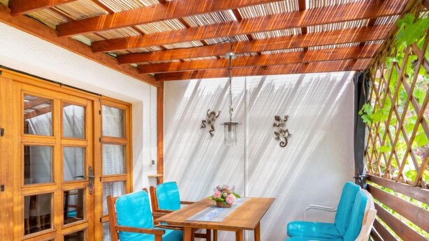 Una mesa de comedor de madera con sillas azules, un aparador de madera con puertas de cristal y una pérgola con diseño de celosía.