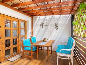 Une table de salle à manger en bois, avec des chaises bleues, un buffet en bois doté de portes en verre et une pergola ornée d’un motif en treillis.