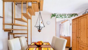 Un comedor con una mesa de madera, sillas blancas, un frutero y una lámpara colgante.