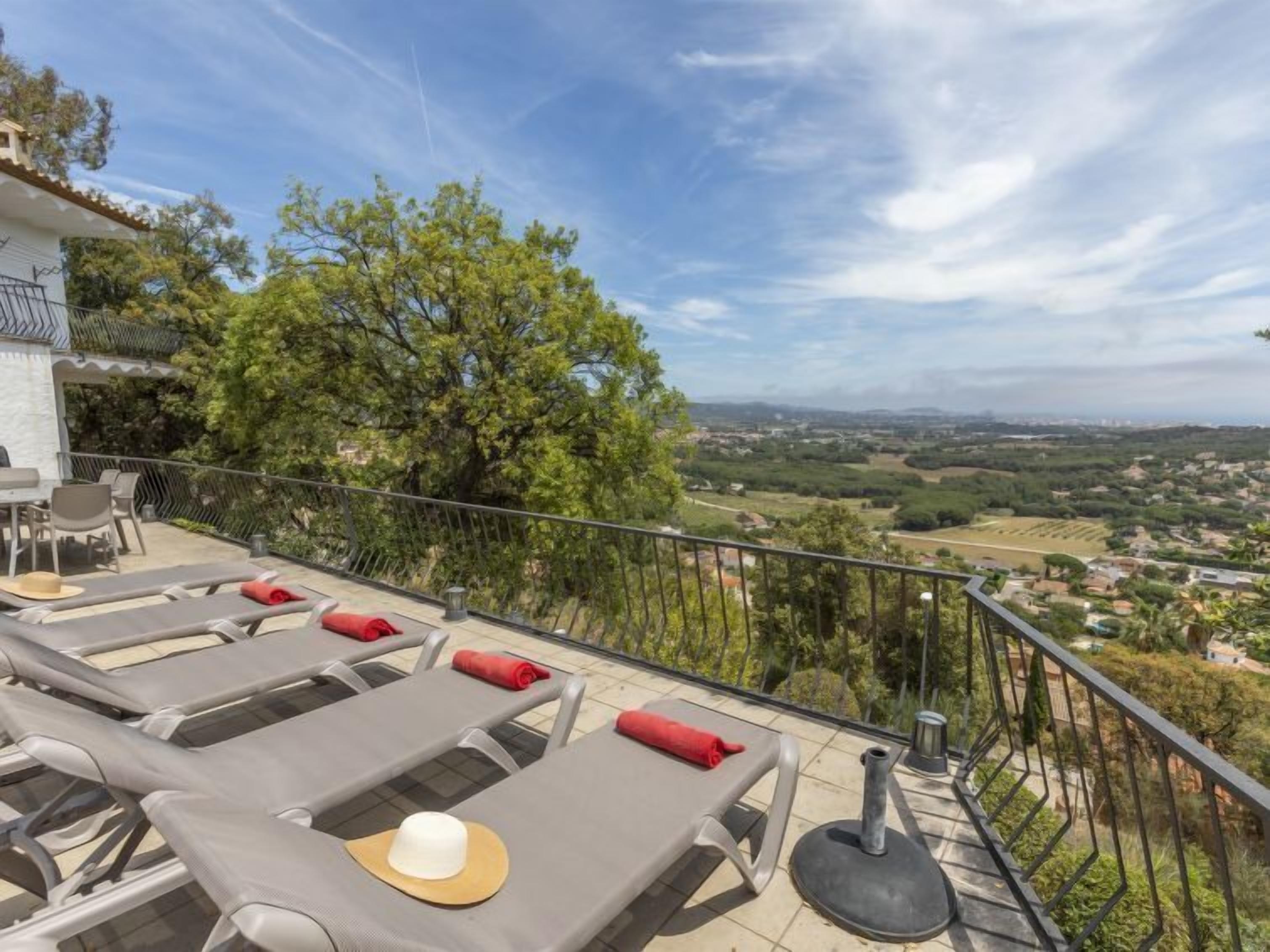 A terrace with sun loungers, a table, and chairs, overlooking a scenic landscape.