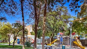 Un parque infantil con toboganes y estructuras para escalar, rodeado de árboles y un edificio al fondo.