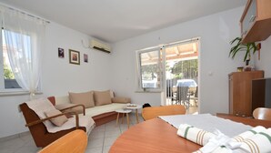 Una habitación acogedora con un sofá, una mesa de comedor y un televisor. Hay una ventana con persianas y una planta en la pared.