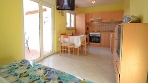 Et kompakt køkken med træskabe, et spiseområde med bord og stole, samt et fjernsyn monteret på væggen.
