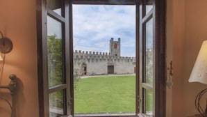 Eine geöffnete Tür, die in einen Innenhof mit einer historischen Steinmauer und einem Turm führt.