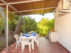 Relax in a serene outdoor space surrounded by lush greenery and a shaded pergola, perfect for dining al fresco.
