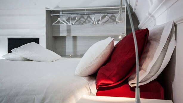 A modern hotel room with a neatly made bed, a bedside table, and a hanging light fixture.