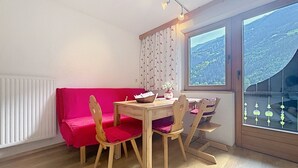 Ein Zimmer mit Holztisch, Stühlen, einem roten Sofa, einem Fenster mit Bergblick und einer Heizung.