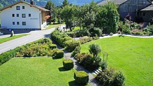 Ein Hotel mit weißer Fassade, einem Garten mit ordentlich geschnittenen Hecken und einer Bergkulisse im Hintergrund.