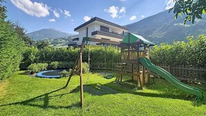 Ein Spielplatz mit Schaukeln und Rutsche, ein Schwimmbecken und ein Haus mit Balkon.
