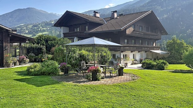 Ein großes Chalet mit Terrasse, umgeben von üppiger Vegetation und Bergen.