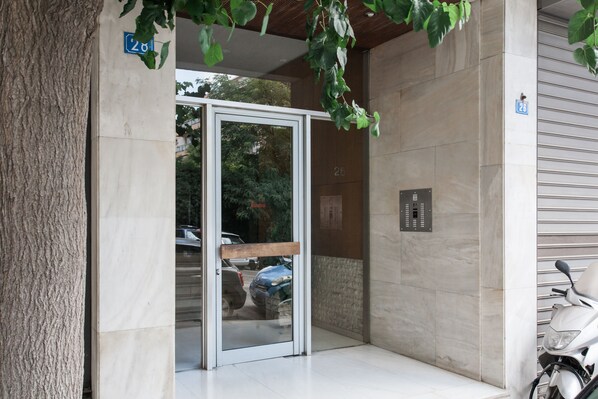 A building entrance with a glass door, a wooden bench, and a scooter parked outside.