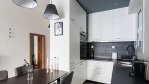 A modern kitchen with white cabinets, a black countertop, and a dining area with a dark table and chairs. - UPSTREET Charming & Comfy 2BD Apt-Acropolis (Athens)