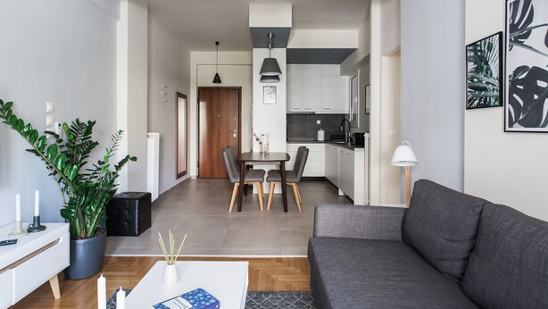 A modern living room with a grey sofa, a white coffee table, and a dining area with a wooden table and chairs. - UPSTREET Charming & Comfy 2BD Apt-Acropolis (Athens)