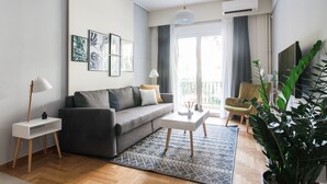 A modern living room with a grey sofa, a white coffee table, a floor lamp, and a large potted plant. - UPSTREET Charming & Comfy 2BD Apt-Acropolis (Athens)