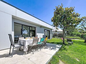 Une maison moderne dotée d’un patio comprenant une table et des chaises, un petit jardin et un arbre.