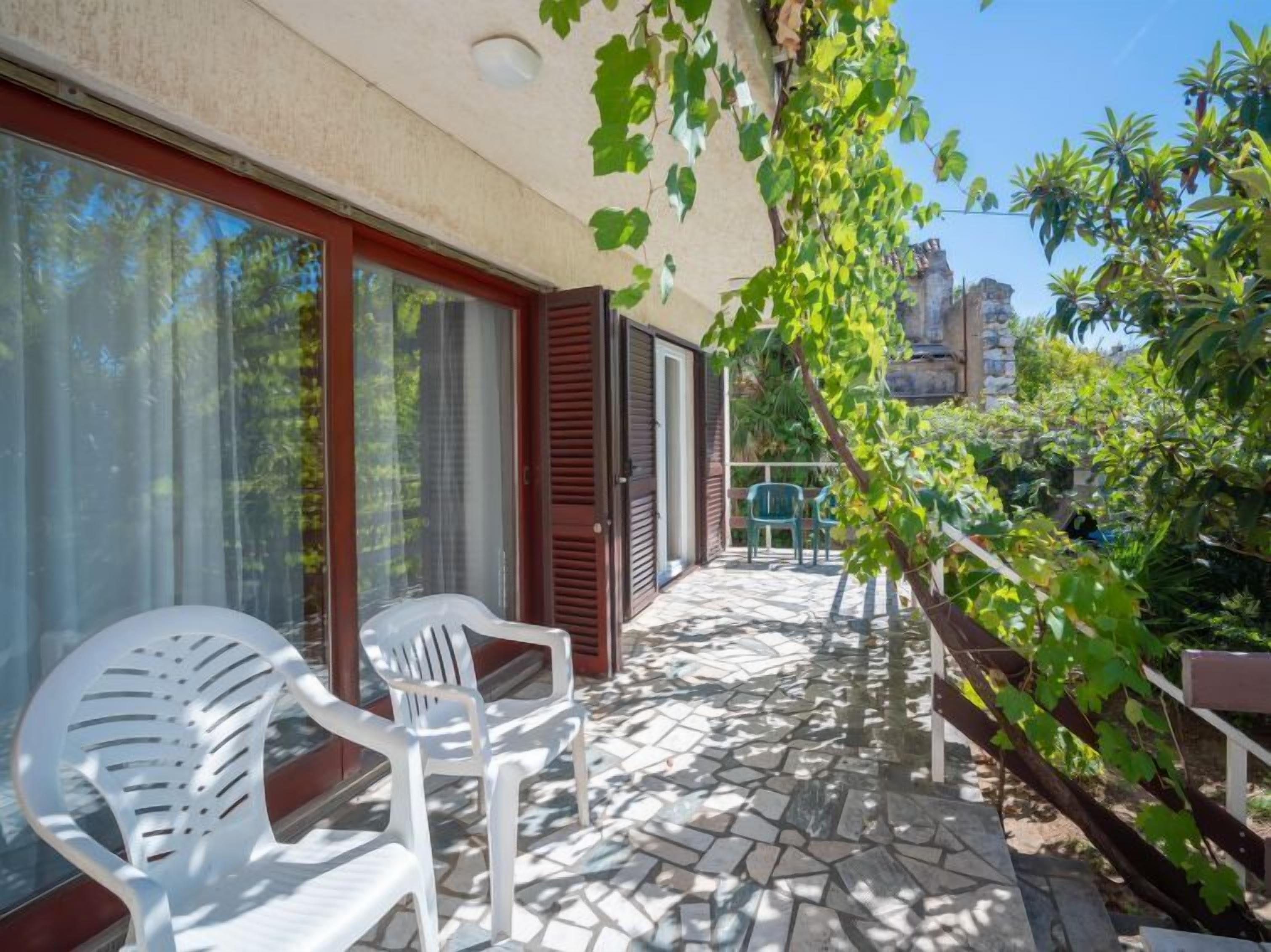 Eine Terrasse mit zwei weißen Plastikstühlen, einem gefliesten Boden und Blick auf ein Gebäude im Hintergrund.