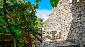 A stone-walled outdoor area with a tiled patio, a wooden bench, and a table with chairs. - Andrijana by Interhome (Novi Vinodolski)