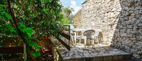 A stone-walled outdoor area with a tiled patio, a wooden bench, and a table with chairs.