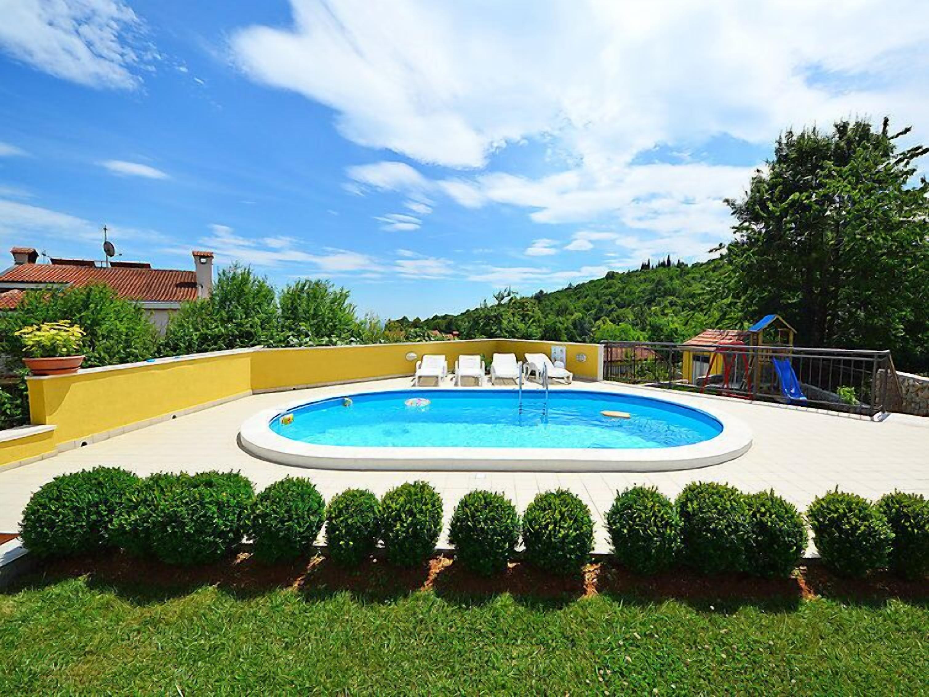 A swimming pool with lounge chairs, surrounded by well-manicured bushes and a playground.