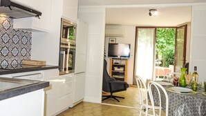 Eine kleine Küche mit weißen Schränken, einer Mikrowelle und einem Herd. Es gibt einen Essbereich mit Tisch, Stühlen und einem Fernseher im Hintergrund.