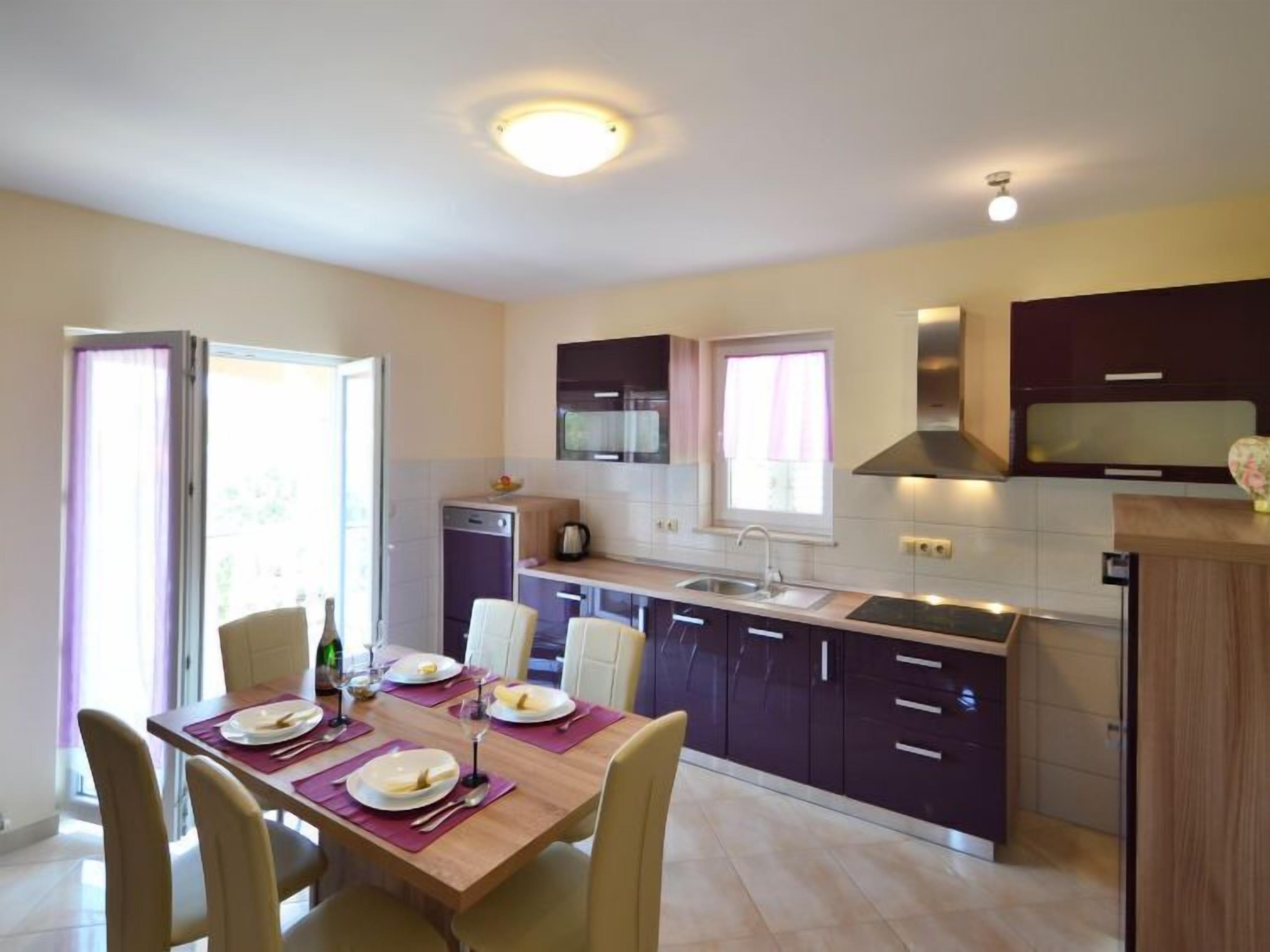 Cocina moderna con comedor, que incluye horno empotrado, pileta y ventana con cortinas.