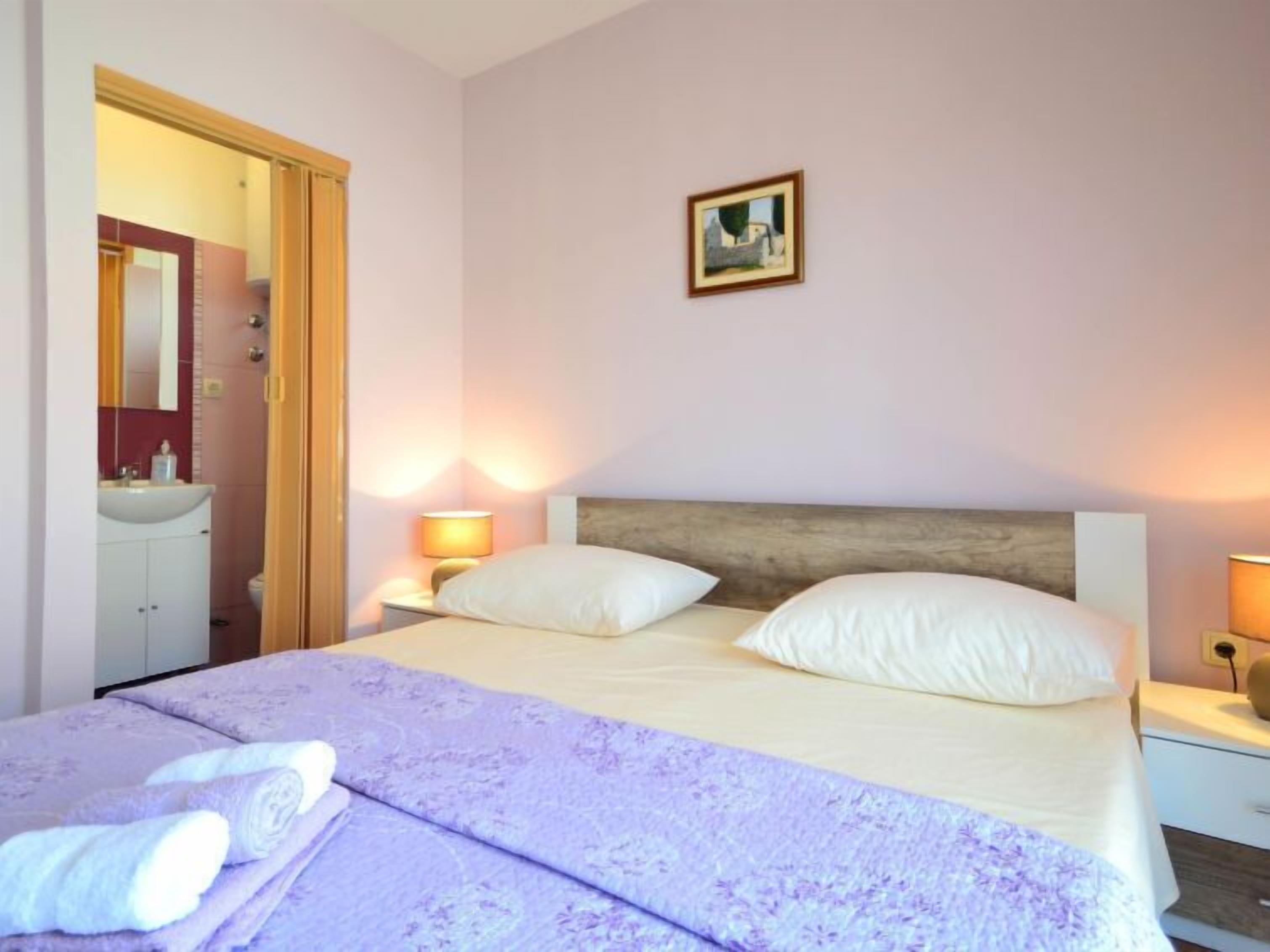 A bedroom with a bed, two bedside lamps, a nightstand, a mirror, and a painting on the wall.