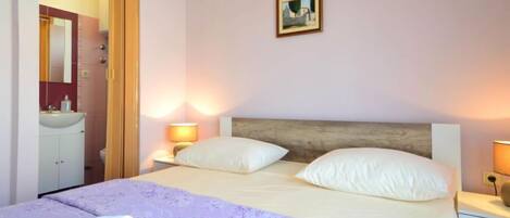 A bedroom with a bed, two bedside lamps, a nightstand, a mirror, and a painting on the wall.