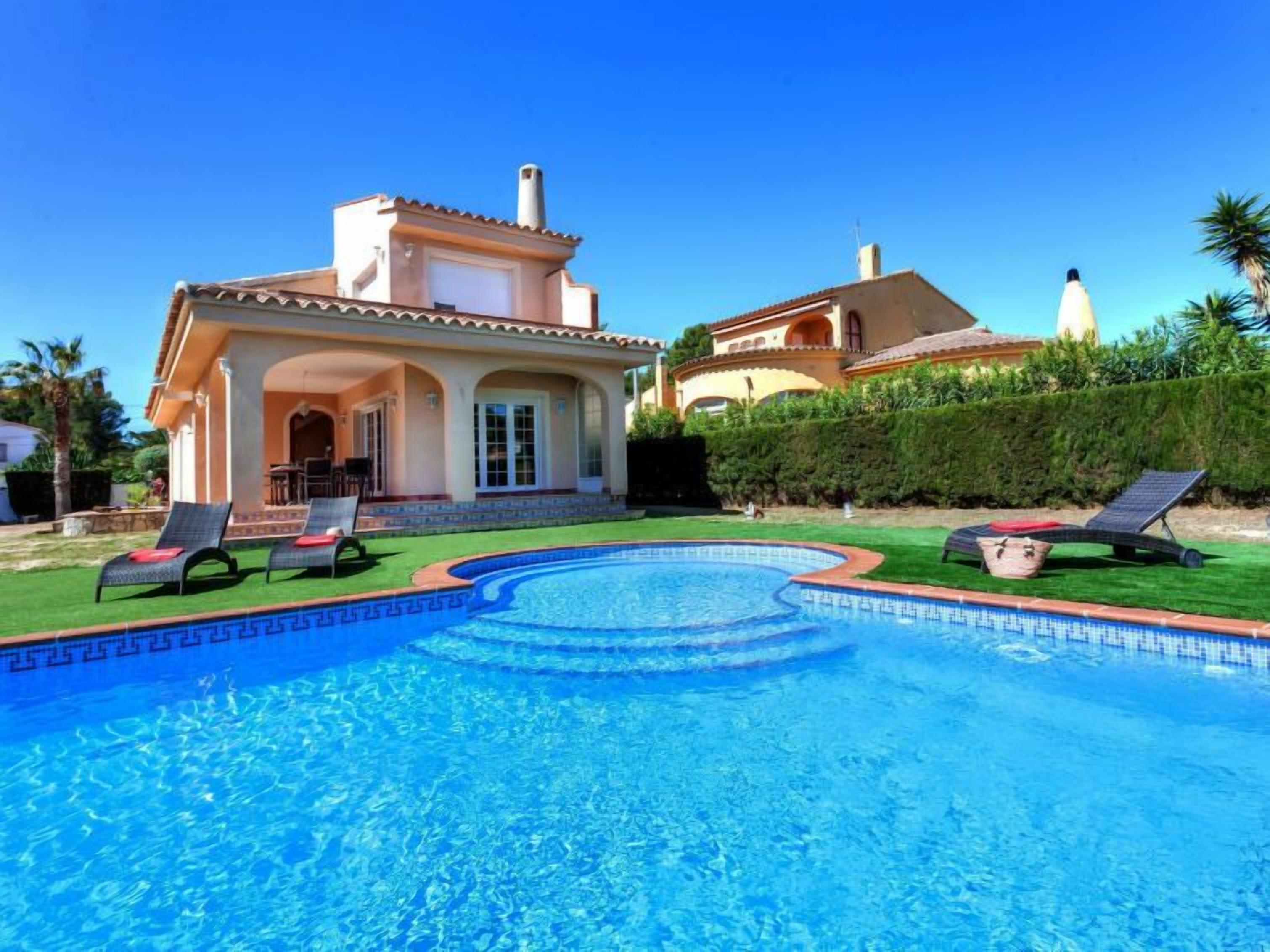 Una casa con piscina, sillas de descanso y un césped bien cuidado.