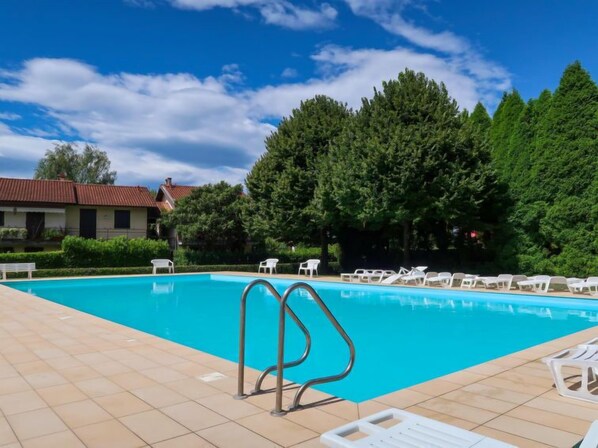 A swimming pool with a metal ladder, surrounded by white lounge chairs and a tiled deck. - Red Sunset by Interhome (Monvalle)