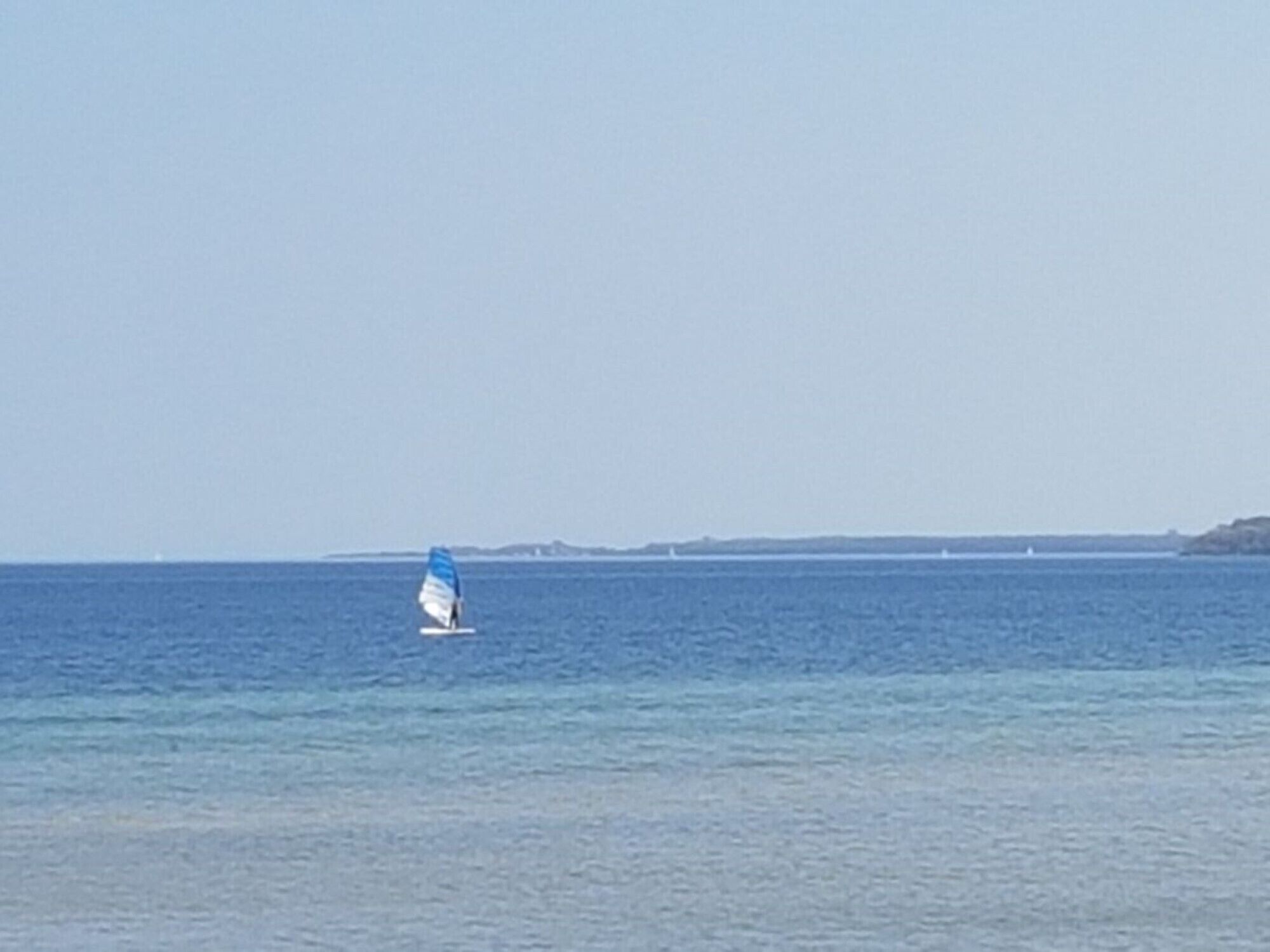 A sailboat on calm waters with a distant shoreline.