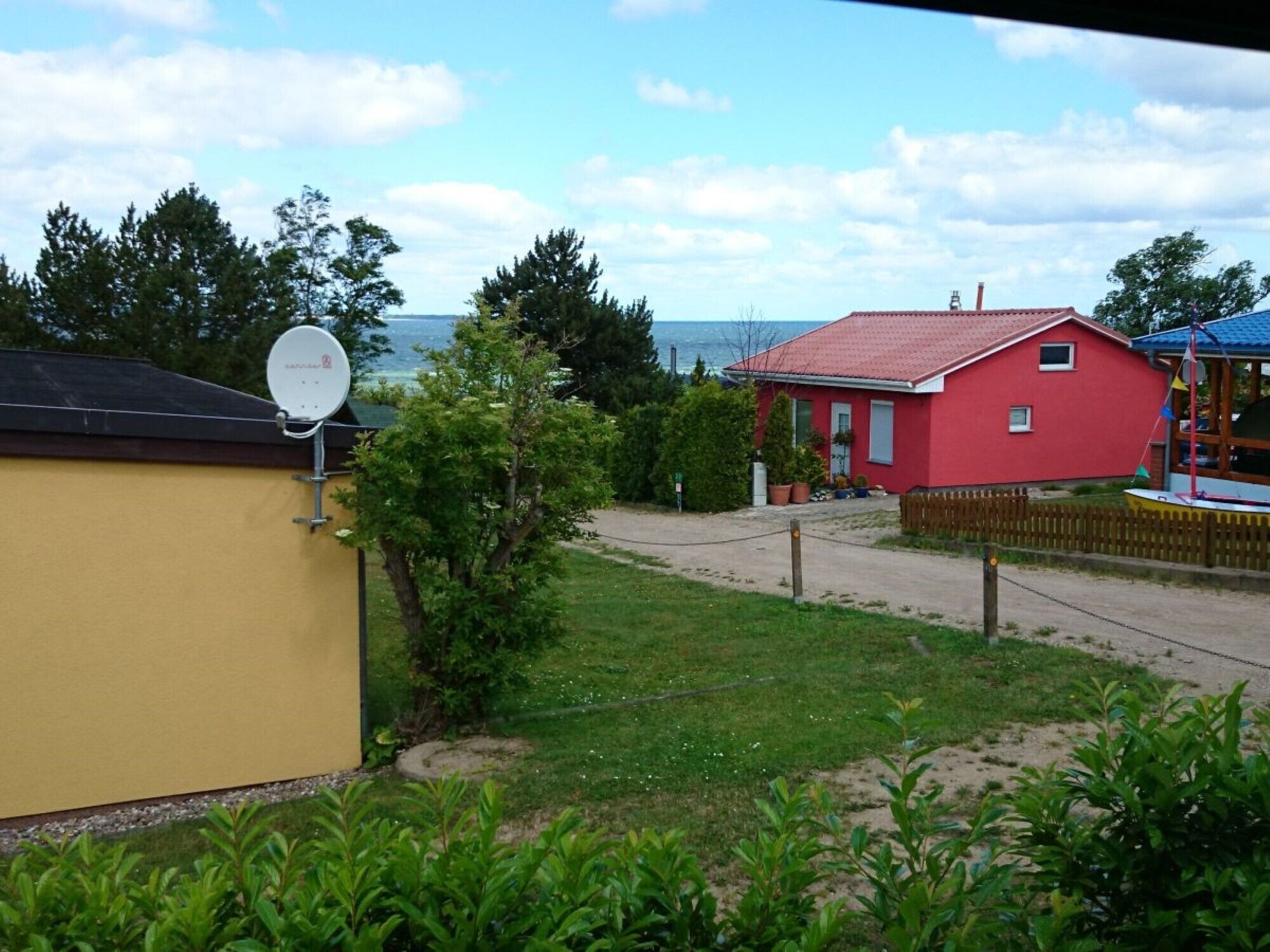 Ein rotes Haus mit Satellitenschüssel, Holzzaun und Meerblick.