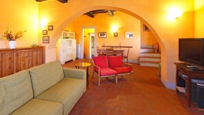 Una sala de estar acogedora con un sofá, un sillón rojo, un televisor y una cocina al fondo.