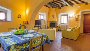 Un comedor con una mesa dispuesta para dos, un sofá y una televisión en una habitación con paredes amarillas y suelo de baldosas.