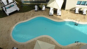 A swimming pool with a wavy edge, surrounded by lounge chairs and umbrellas.