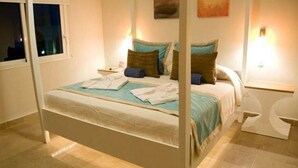 A neatly made bed with pillows and a blanket, a bedside table with a lamp, and a window with curtains.