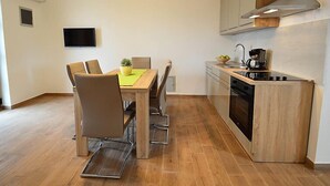 Una cocina compacta con comedor, horno empotrado y televisor montado en la pared.