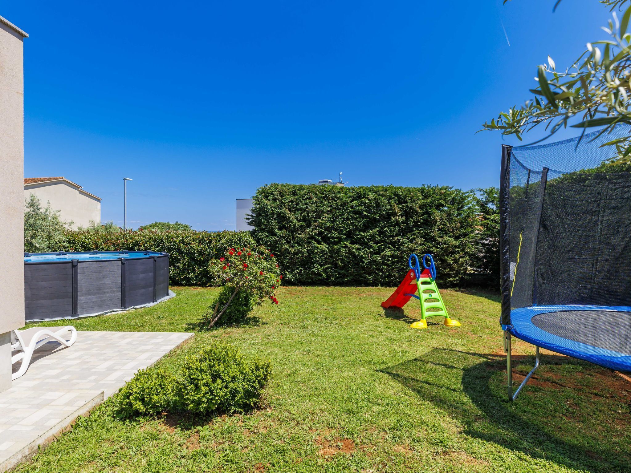 A backyard with a trampoline, a slide, and a small garden area.